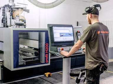 CNC-Herstellung Elemente für Tafelanlagen Operator mit Wittler-Shirt an CNC-Maschine zur Herstellung von Komponenten für Tafelanlagen